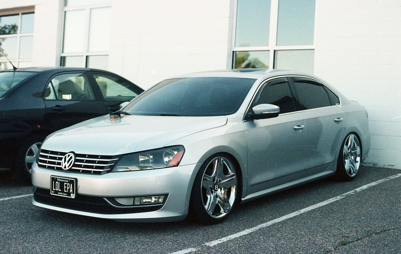 A silver car parked next to a black car in a parking lot